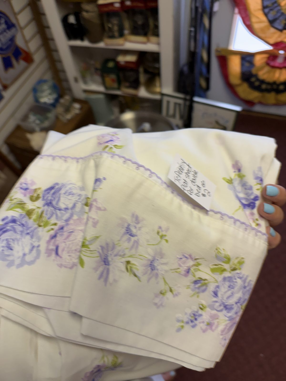 Holding the folded vintage flat sheet at the thrift store in Wisconsin, showing the purple floral cuff and the price tag